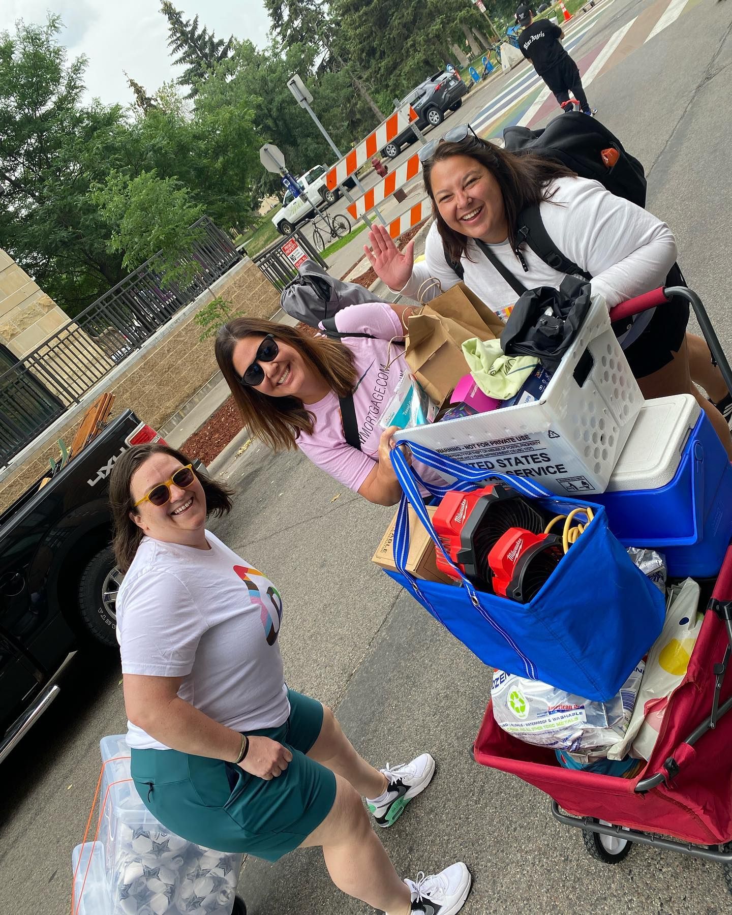 Three women are standing next to a wagon filled with lots of items.