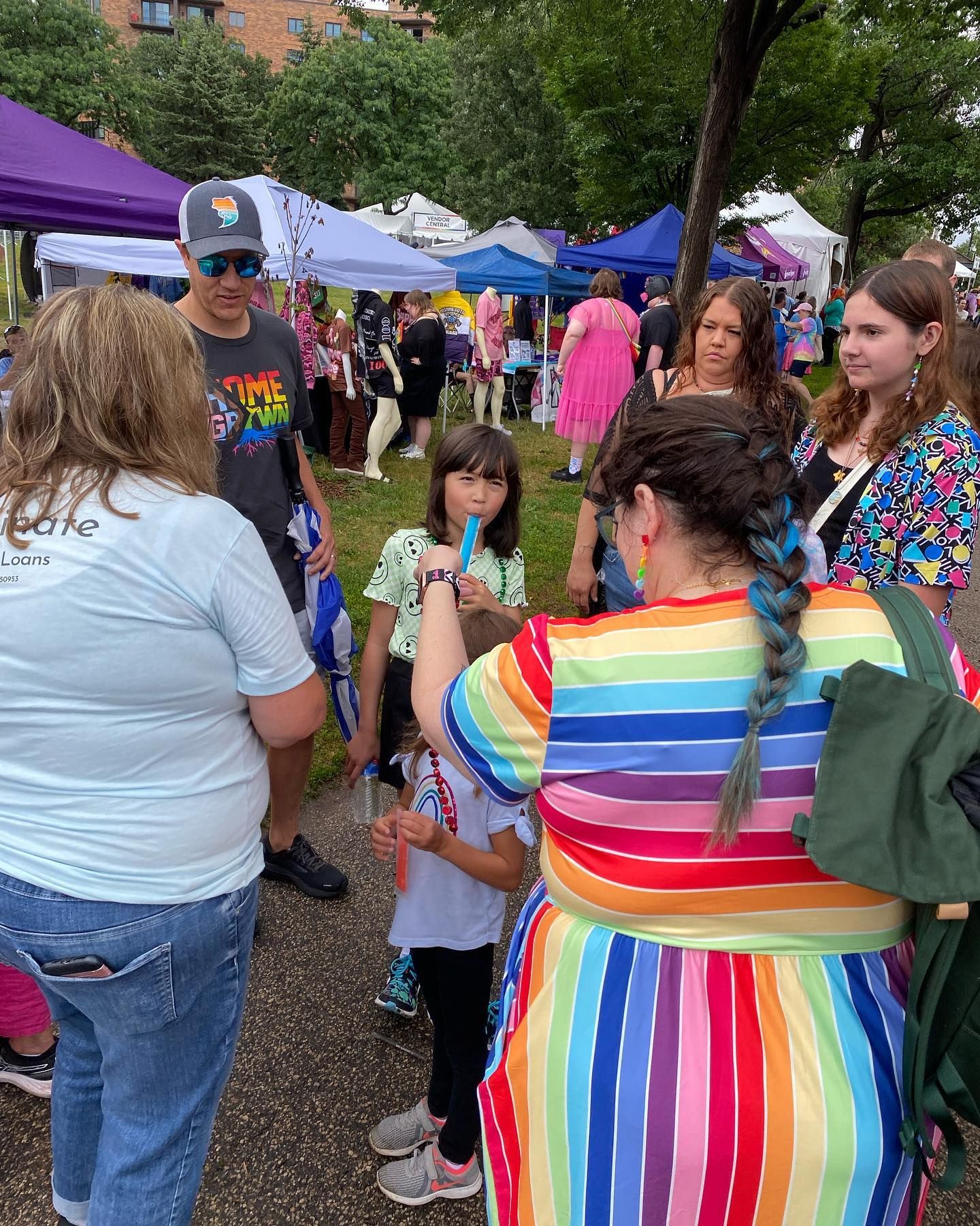 A woman in a rainbow dress is blowing bubbles at a festival.