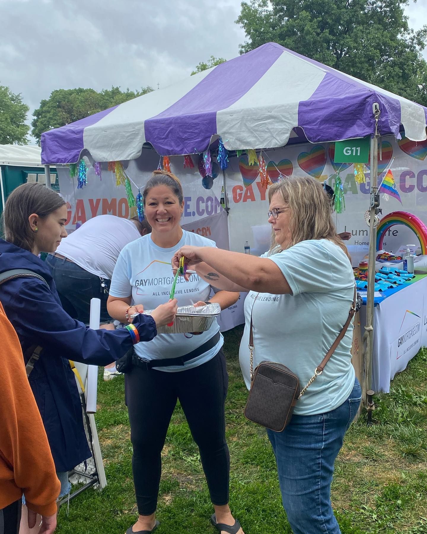 Two women are standing in front of a purple and white tent.