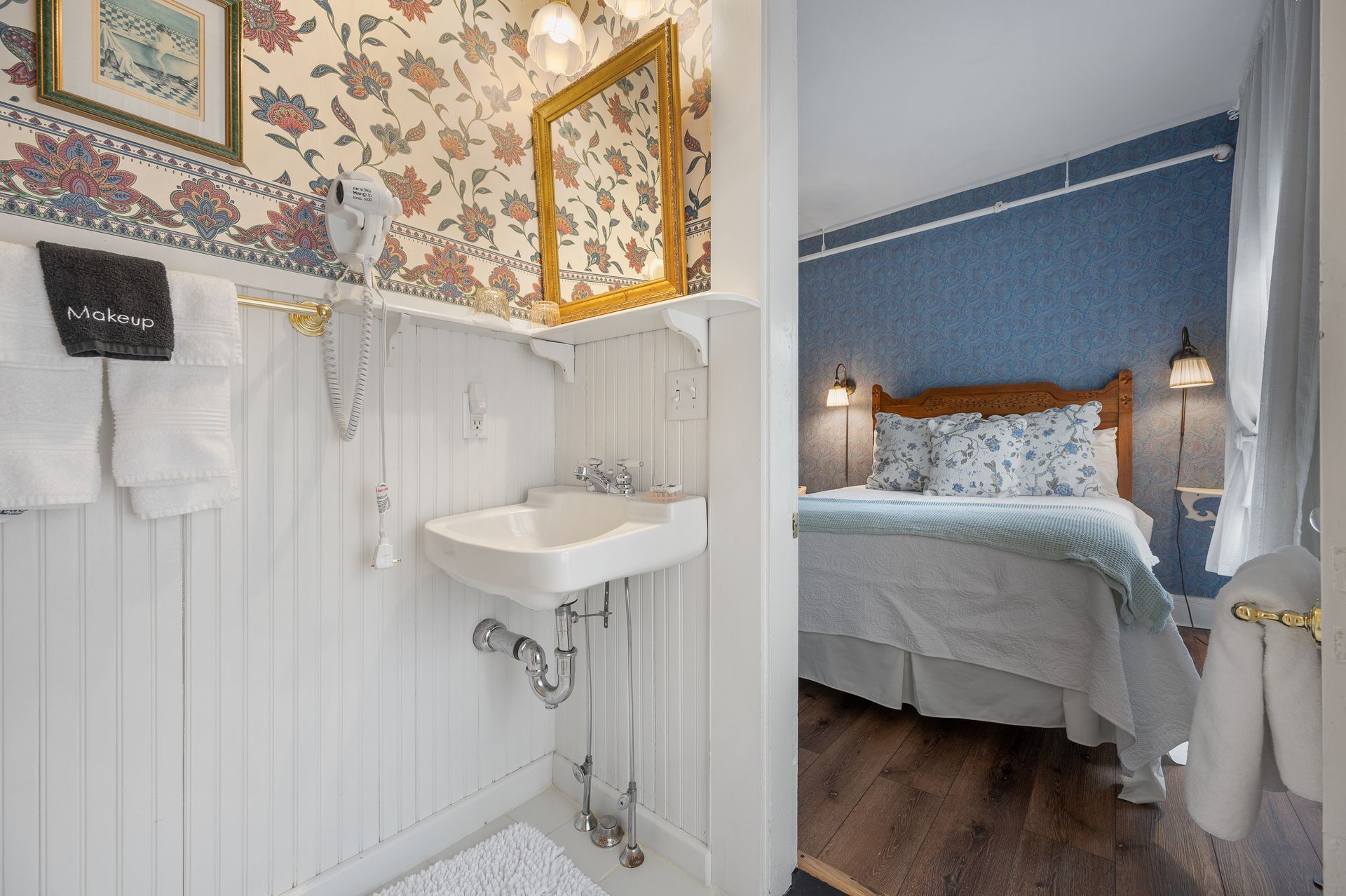 A bathroom with a sink and a mirror next to a bed.