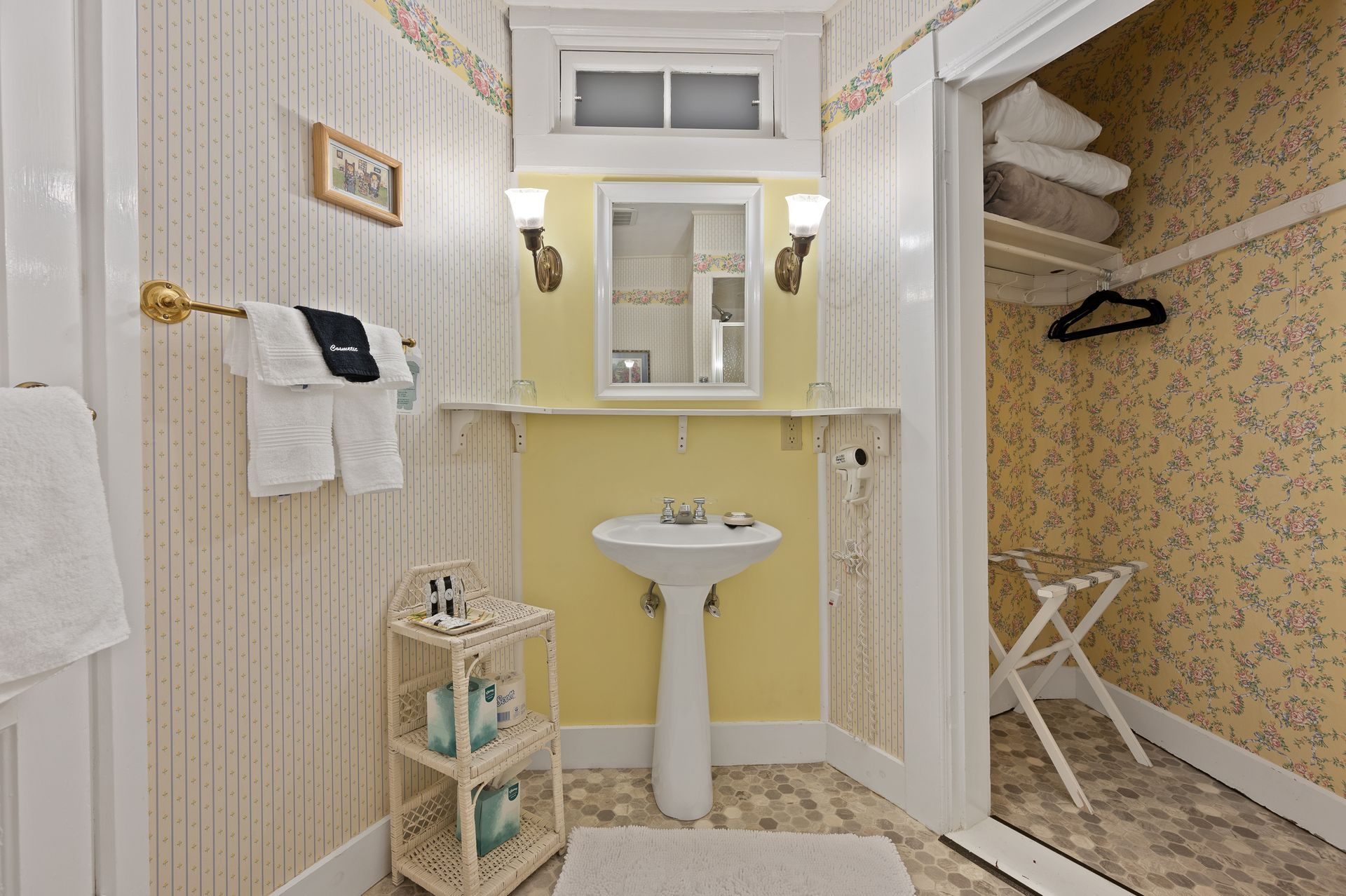 A bathroom with a sink , mirror , towels and a closet.