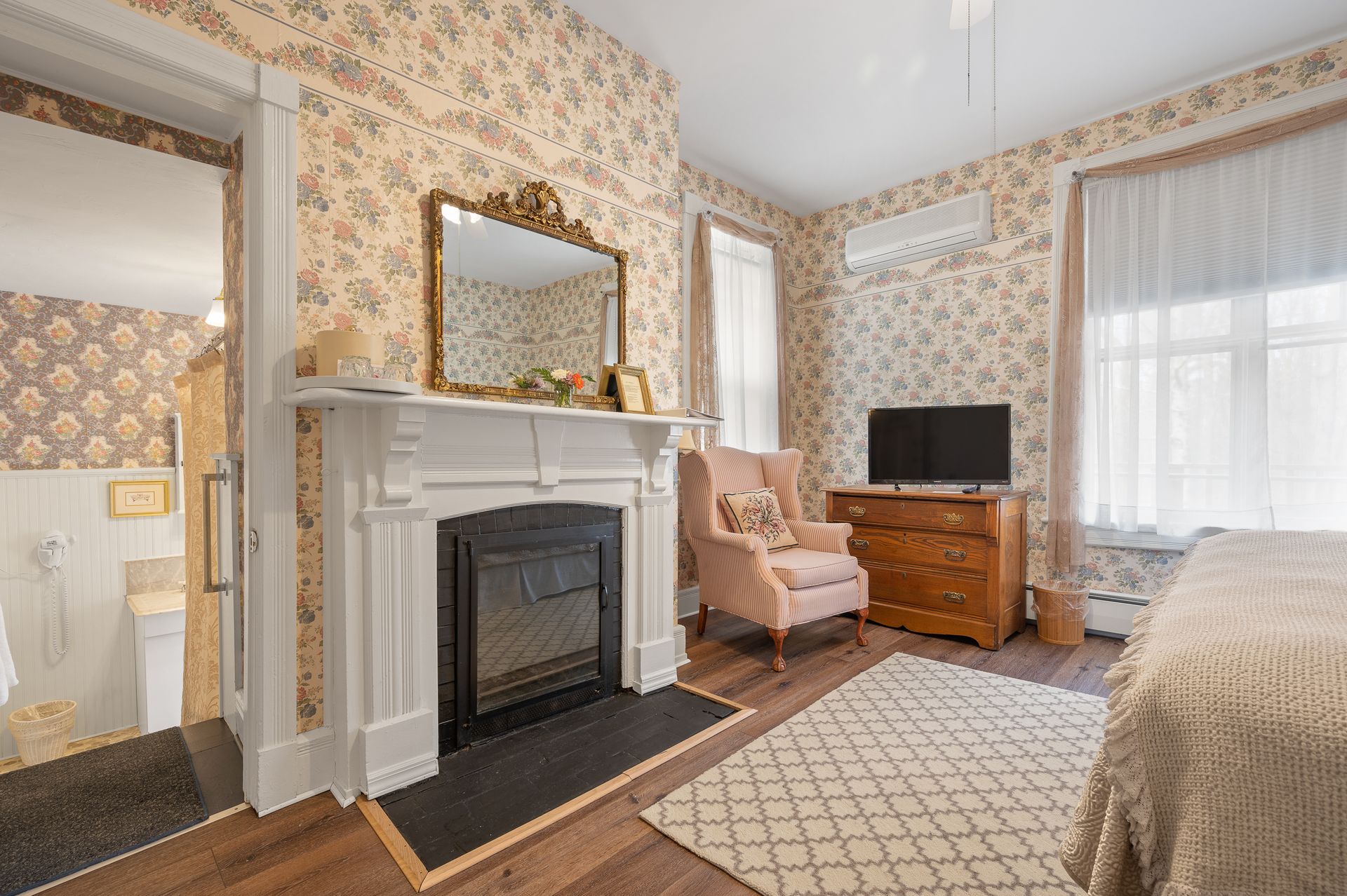 A bedroom with a fireplace , chair , dresser and television.