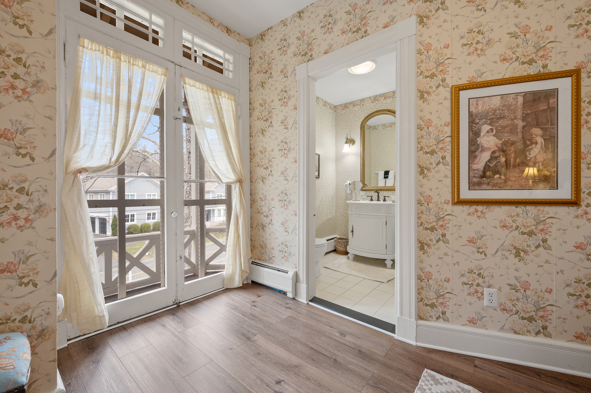 A bedroom with a balcony and a bathroom with a picture on the wall.