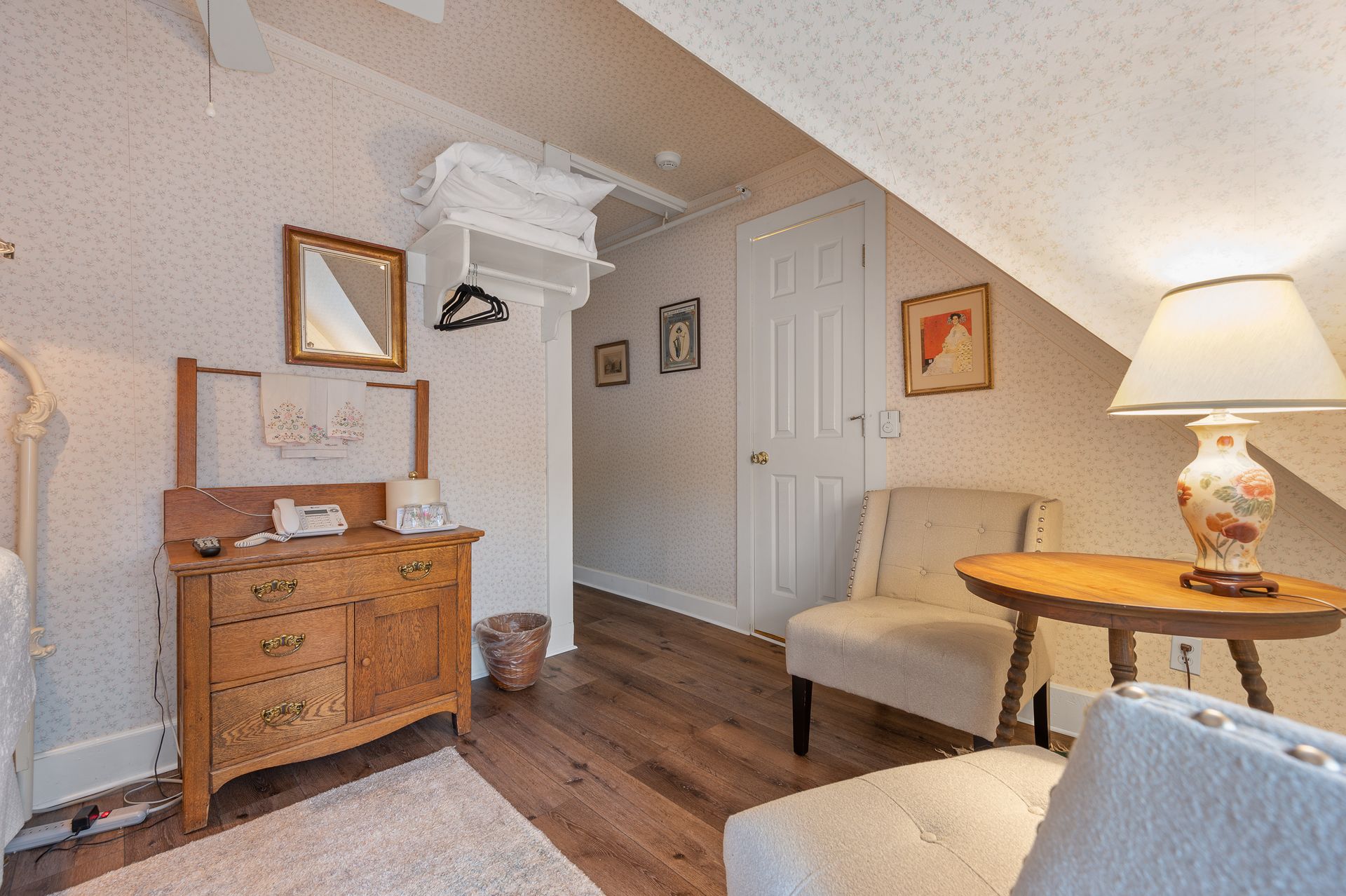 A living room with a dresser , chair , table and lamp.