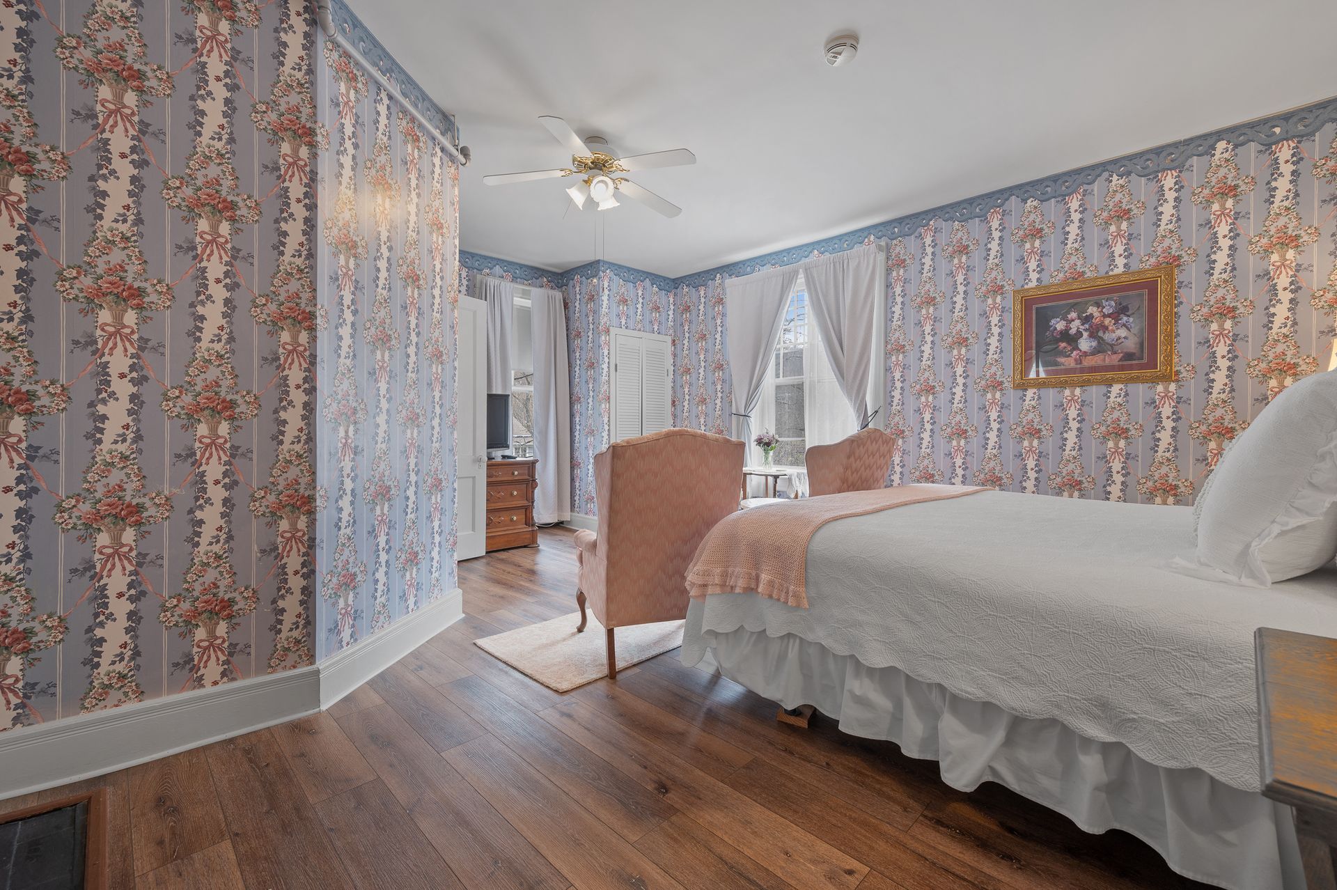 A bedroom with a bed , chair , dresser and ceiling fan.