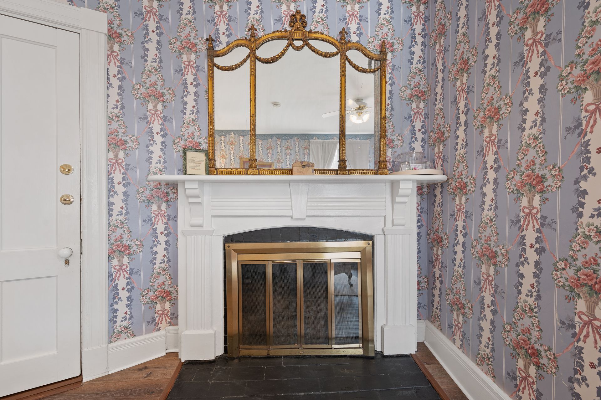A fireplace with a mirror on top of it in a room with floral wallpaper.