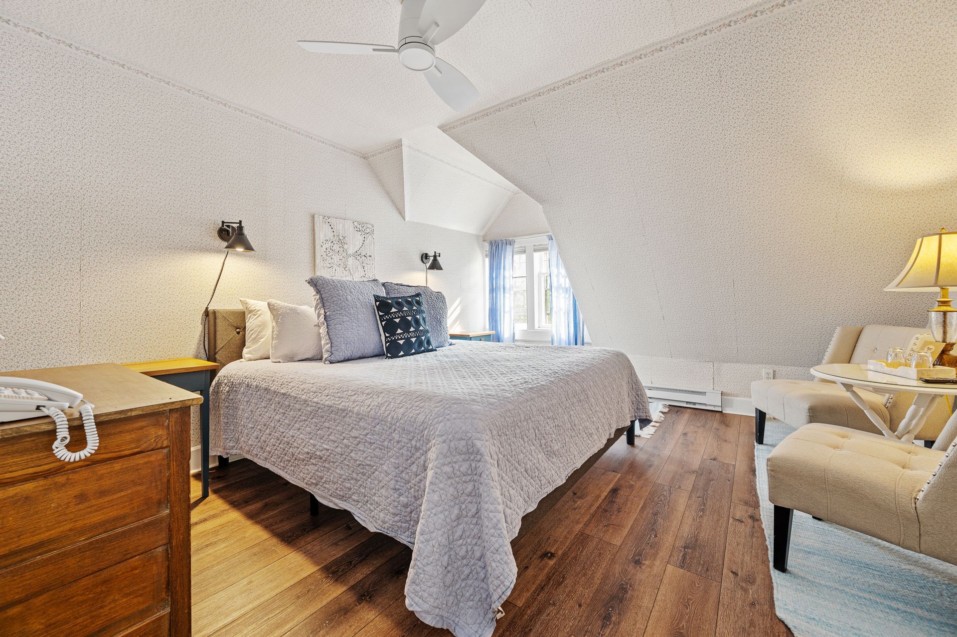 A bedroom with a bed , chairs , dresser and a ceiling fan.