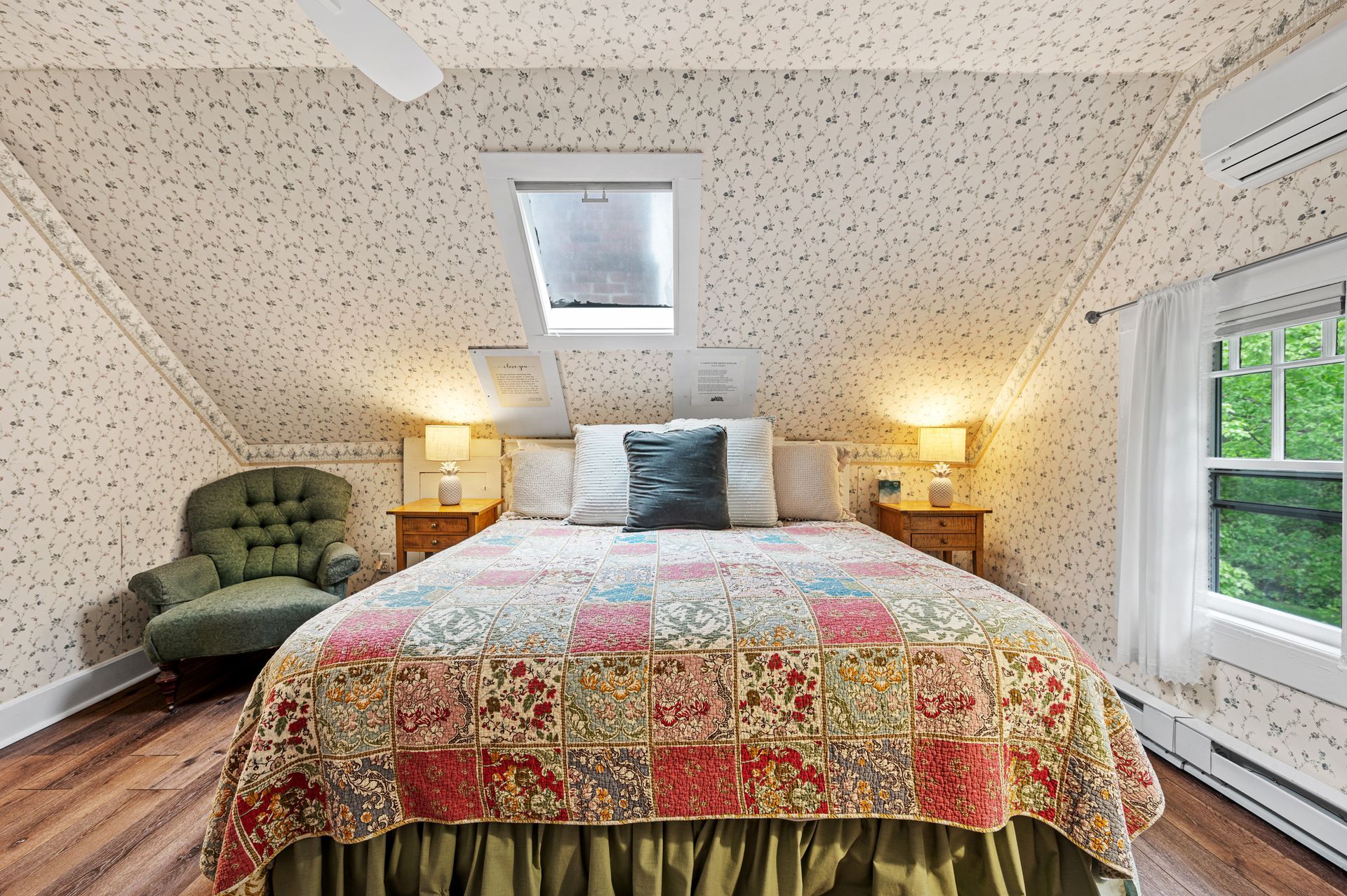 A bedroom with a bed , chair , nightstands and a skylight.