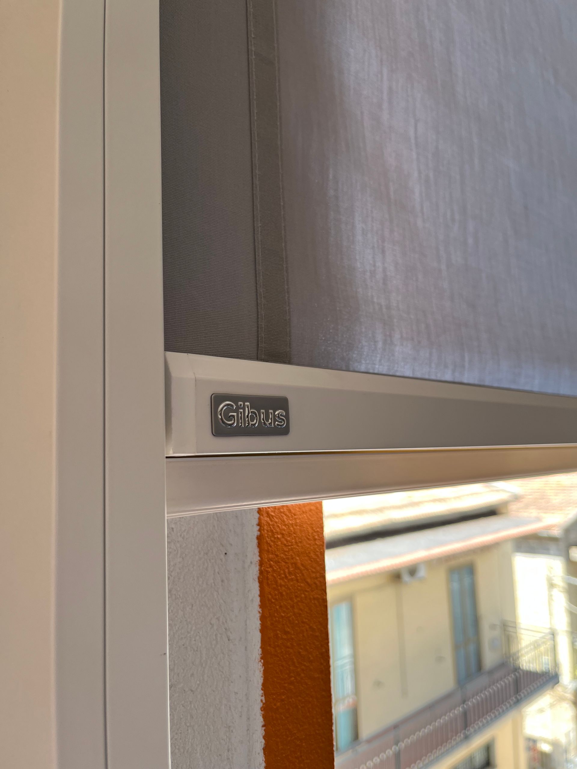 Telaio della finestra bianco con tenda a rullo Gibu grigia.