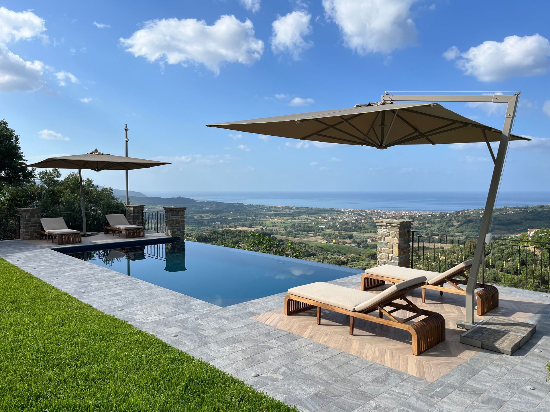 Piscina a sfioro con vista panoramica, dotata di sedie a sdraio e ombrelloni.