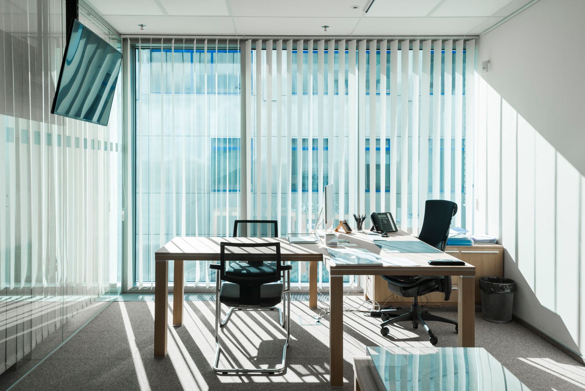 Interno dell'ufficio con scrivania, sedie e tende, luce naturale proveniente dalle finestre.