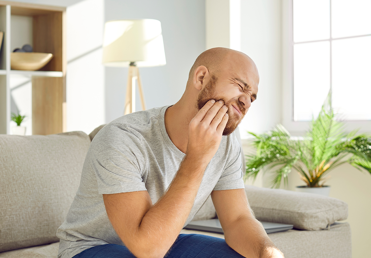 A man is sitting on a couch with a toothache.