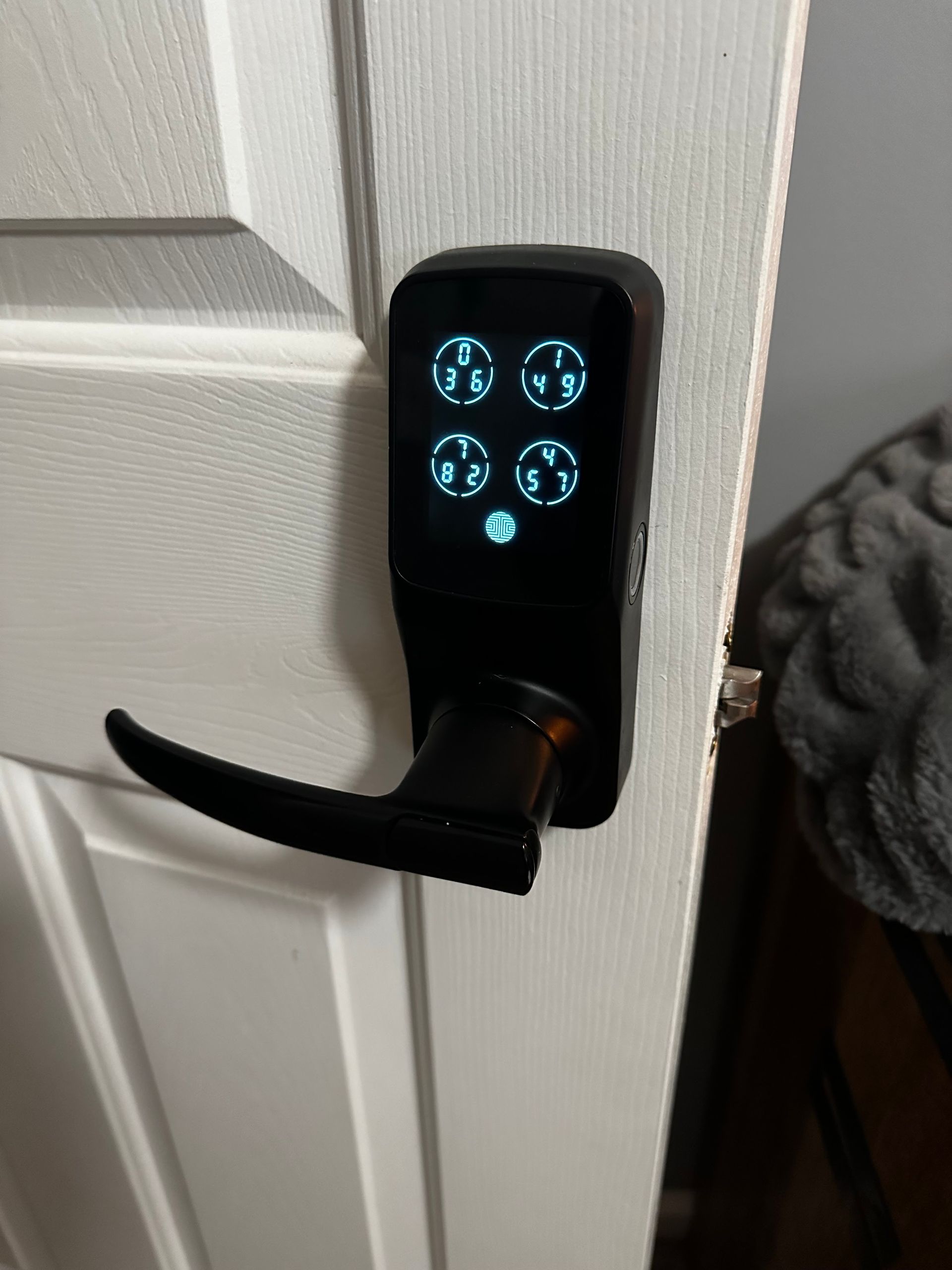 Black smart lock with four number buttons on a white door.