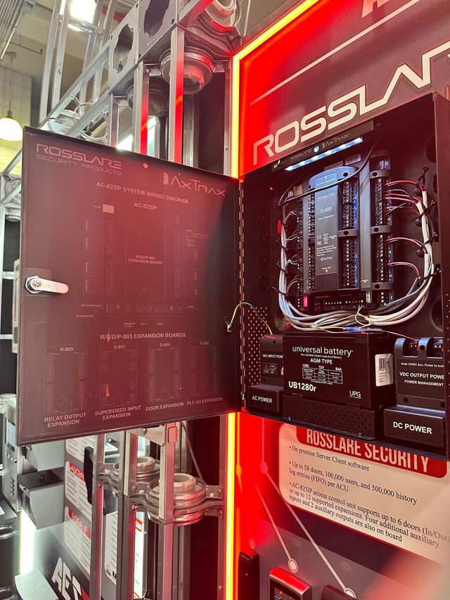 Opened black security system cabinet with wiring and components, mounted on a wall with red accents.