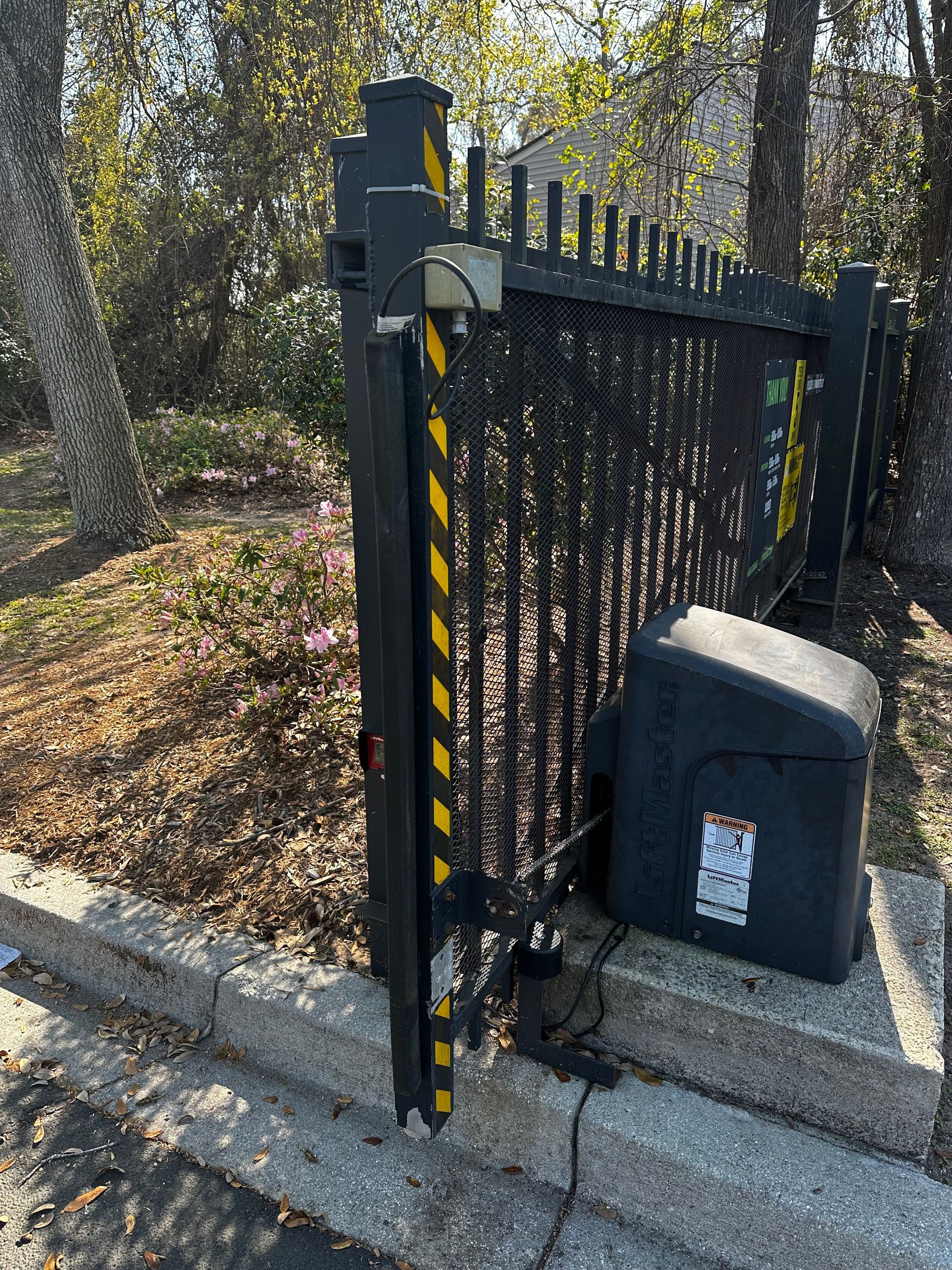 Black automatic gate with safety stripes; motor attached to concrete base near foliage.