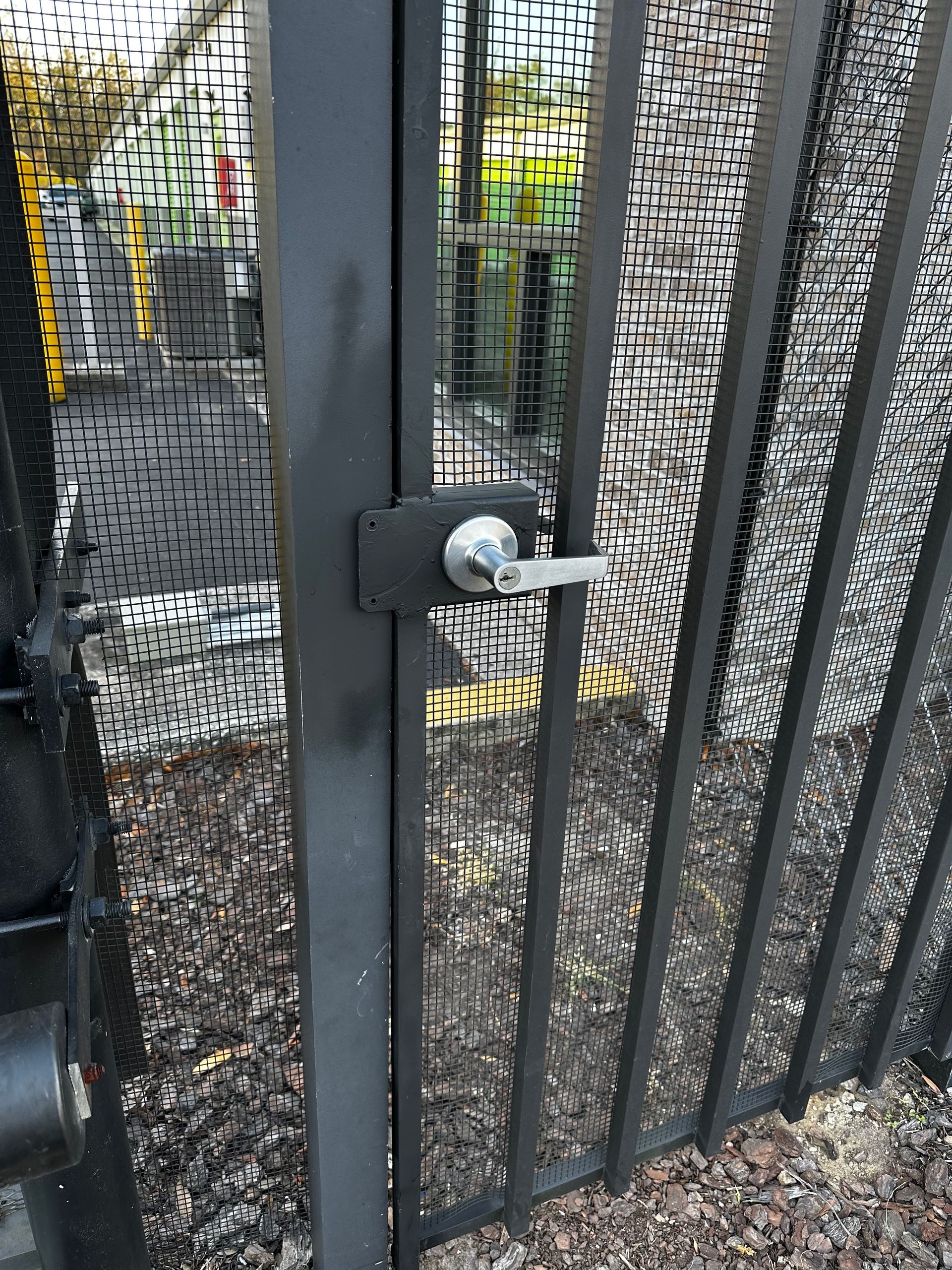 Black metal gate with a silver handle and lock, outdoors.