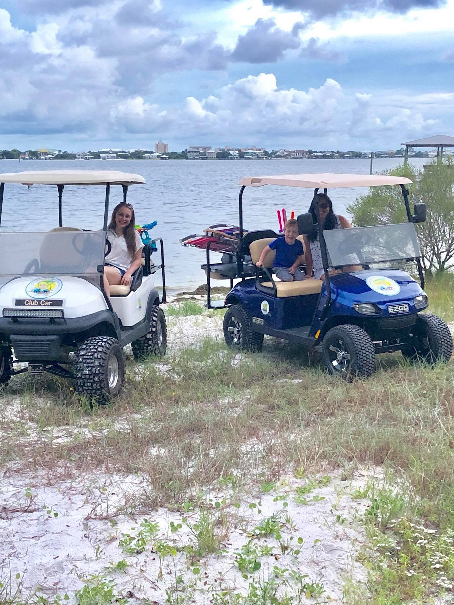 Three people on golf carts by a lakeshore, with cloudy sky and water in the background.