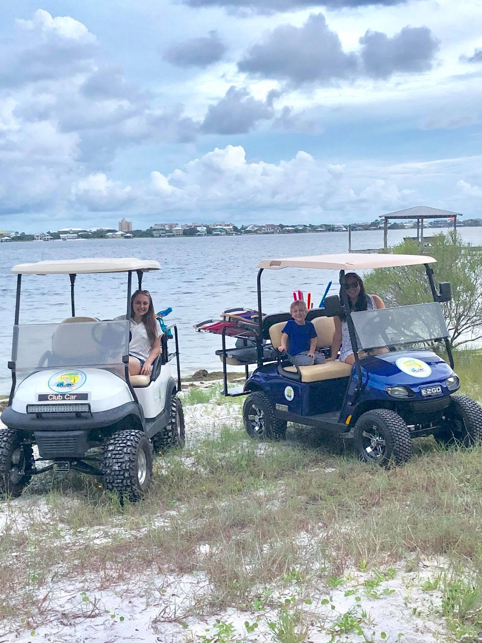 Two golf carts parked by a lakeside under cloudy skies, with two people sitting in them.