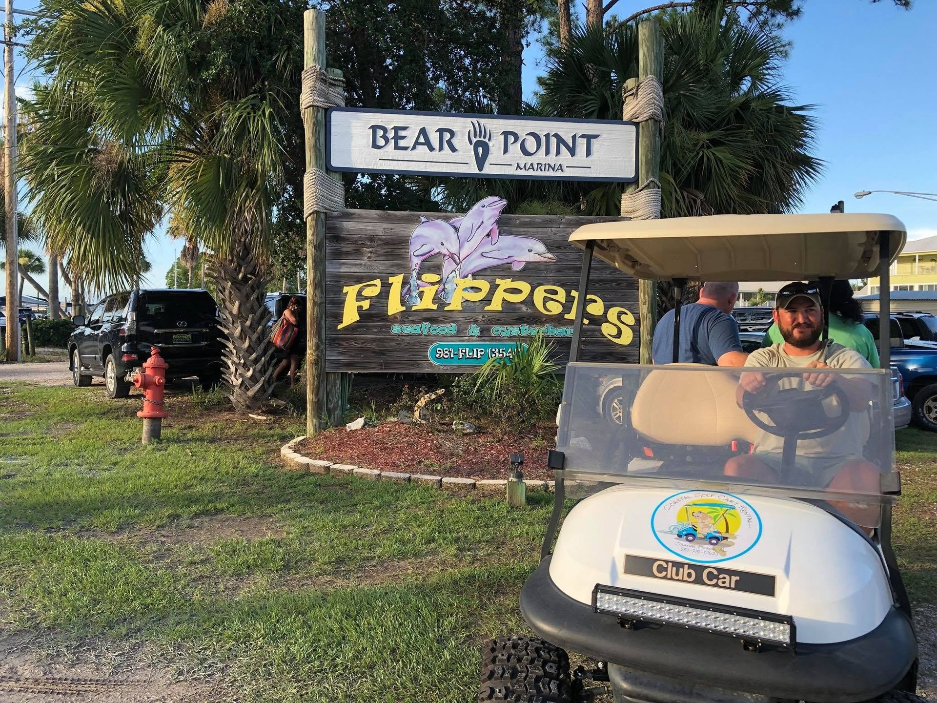 “Flippers” sign at Dear Point entrance with golf cart in front and palm trees in the background