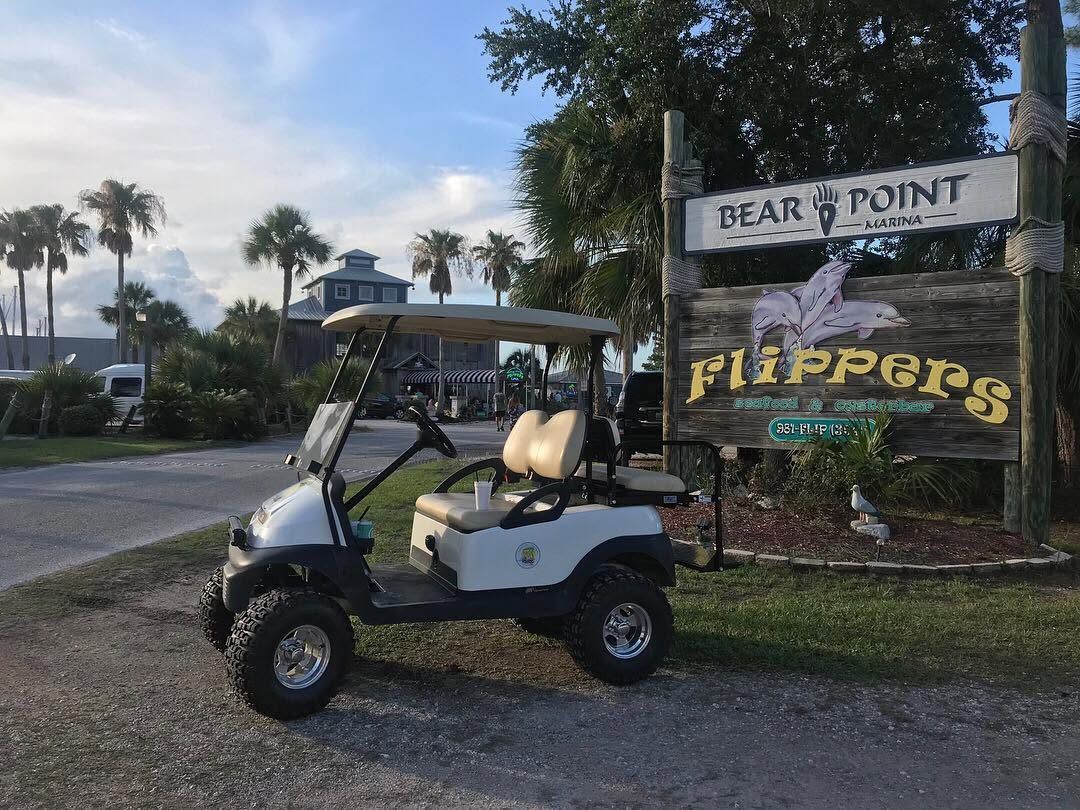 Golf cart parked by a “Gear Point Flippers” sign in a tropical roadside setting