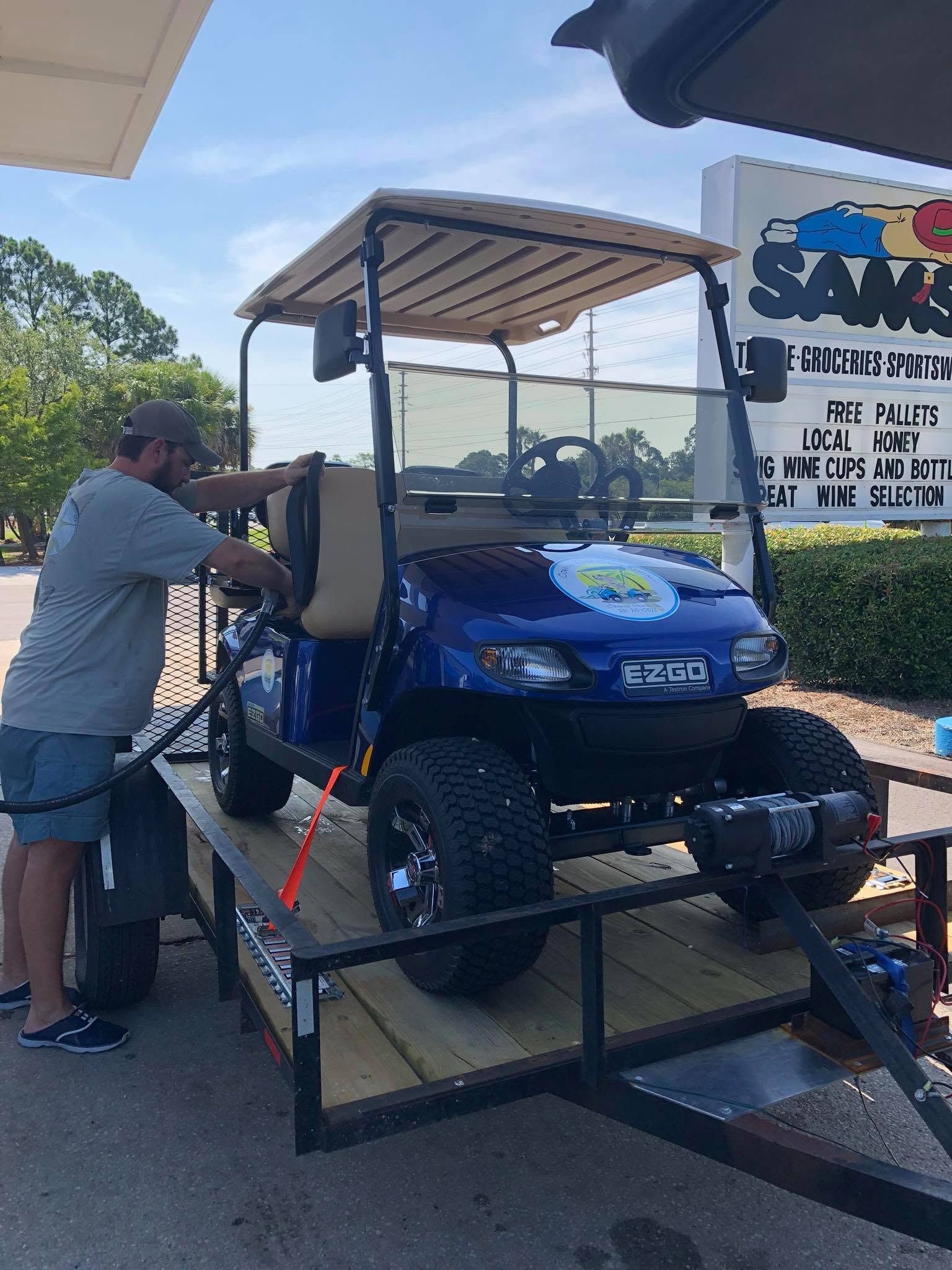 Blue golf cart on a trailer while a person loads items at an outdoor store lot