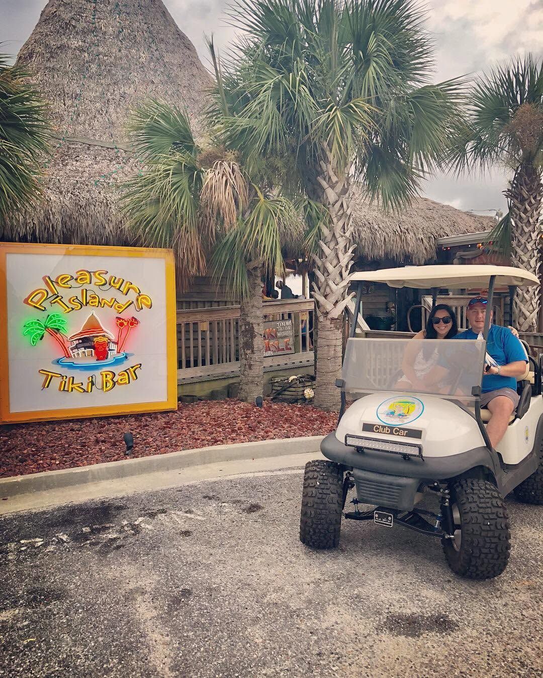 Golf cart beside colorful “Tiki Bar” sign in a tropical resort setting