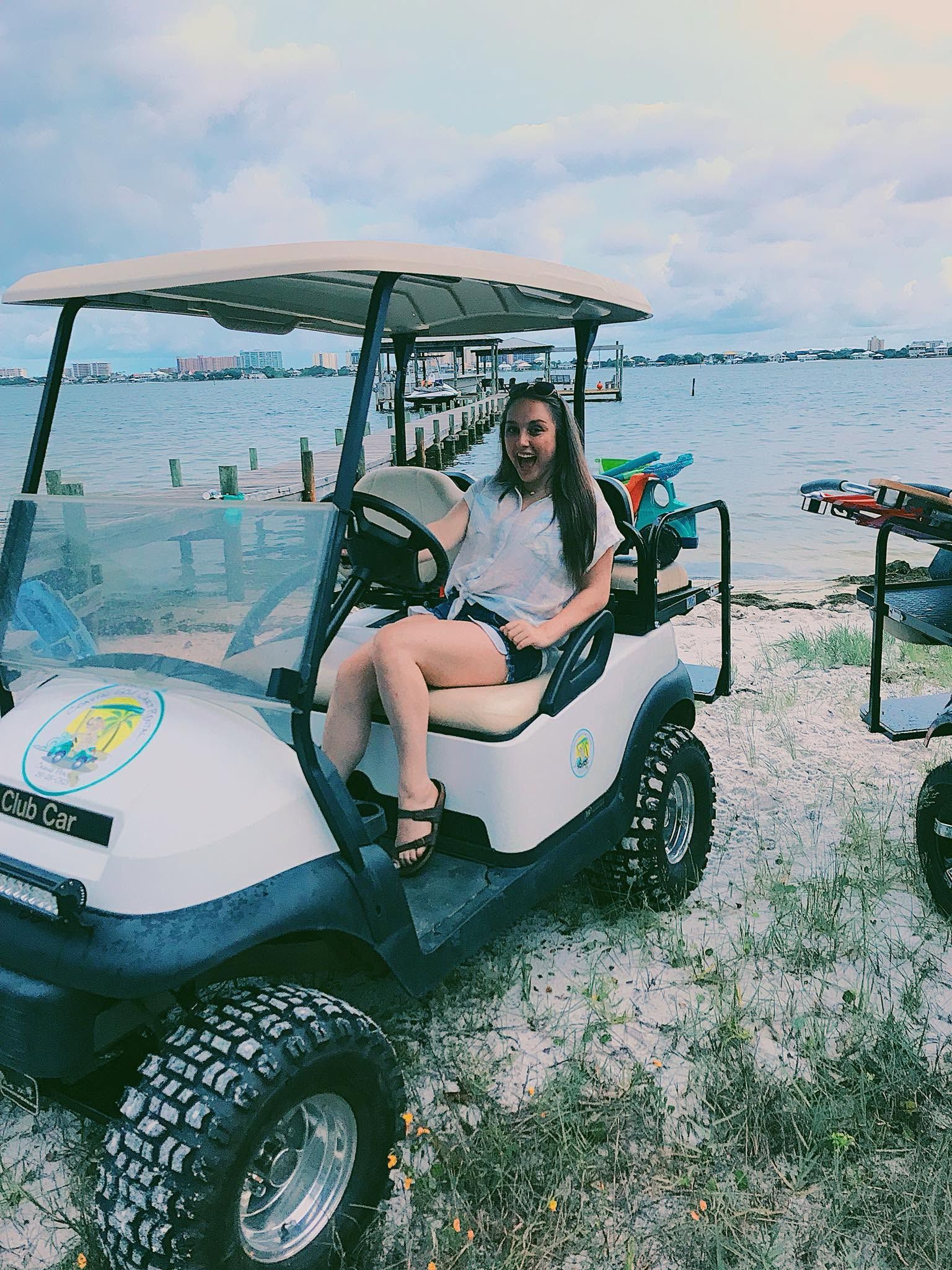Person driving a white golf cart on a rocky beach by the water under a cloudy sky