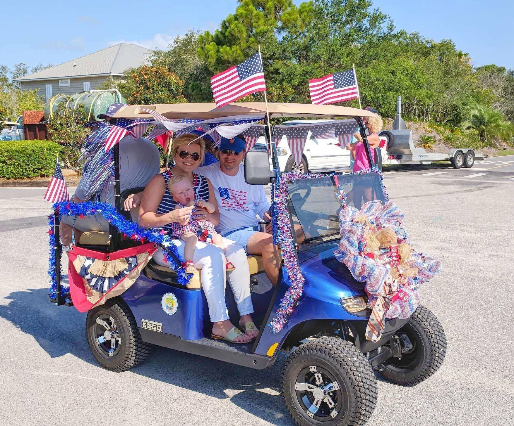 Decorated blue golf cart with passengers and American flags at a sunny parade.