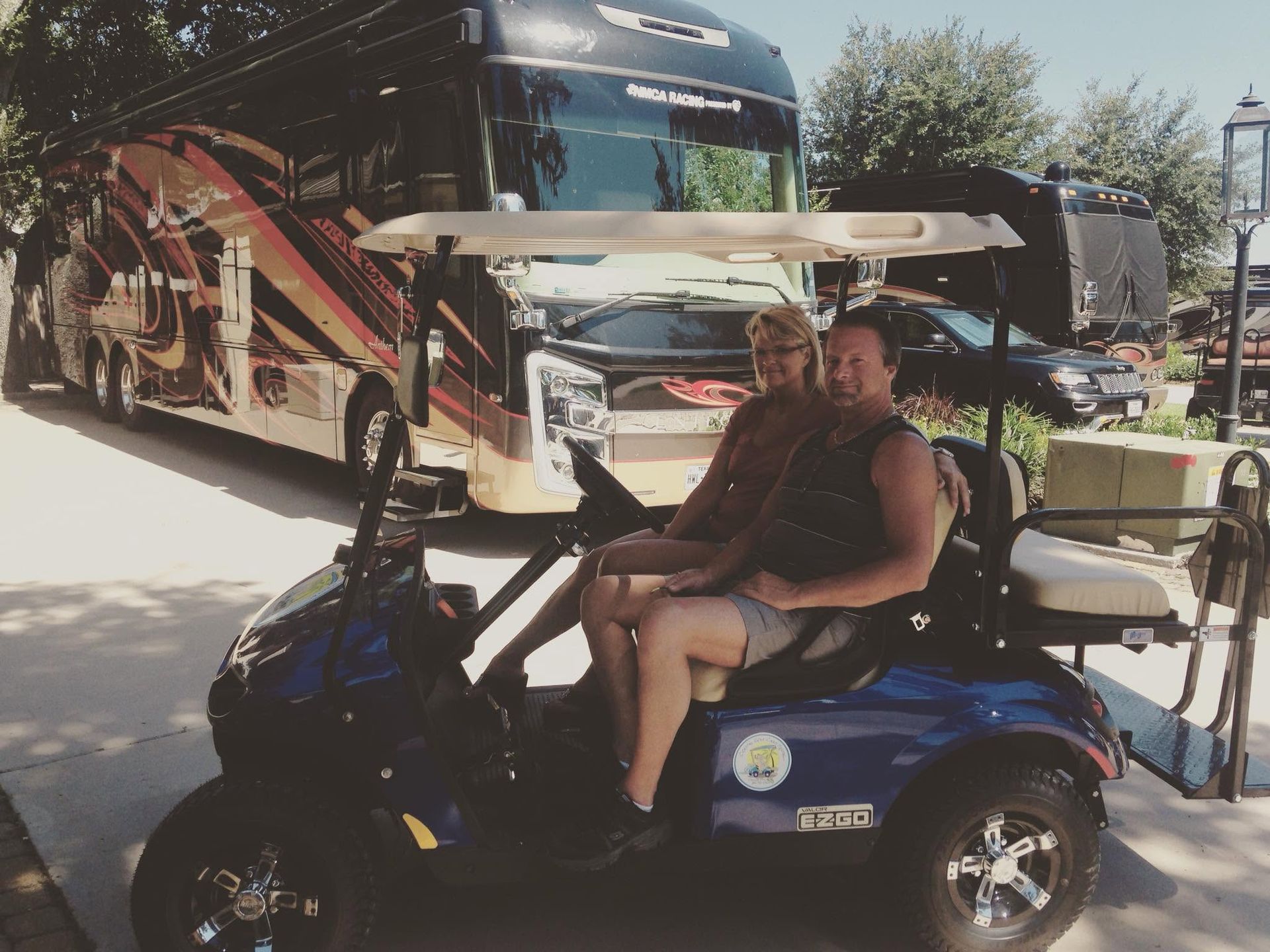 Man sitting on a blue golf cart in front of a large parked bus at an outdoor campsite