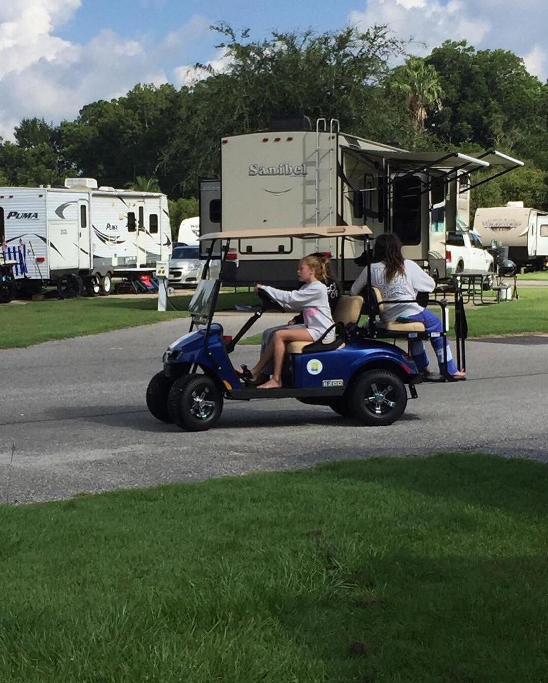Person drives a blue golf cart past RVs at a campground.