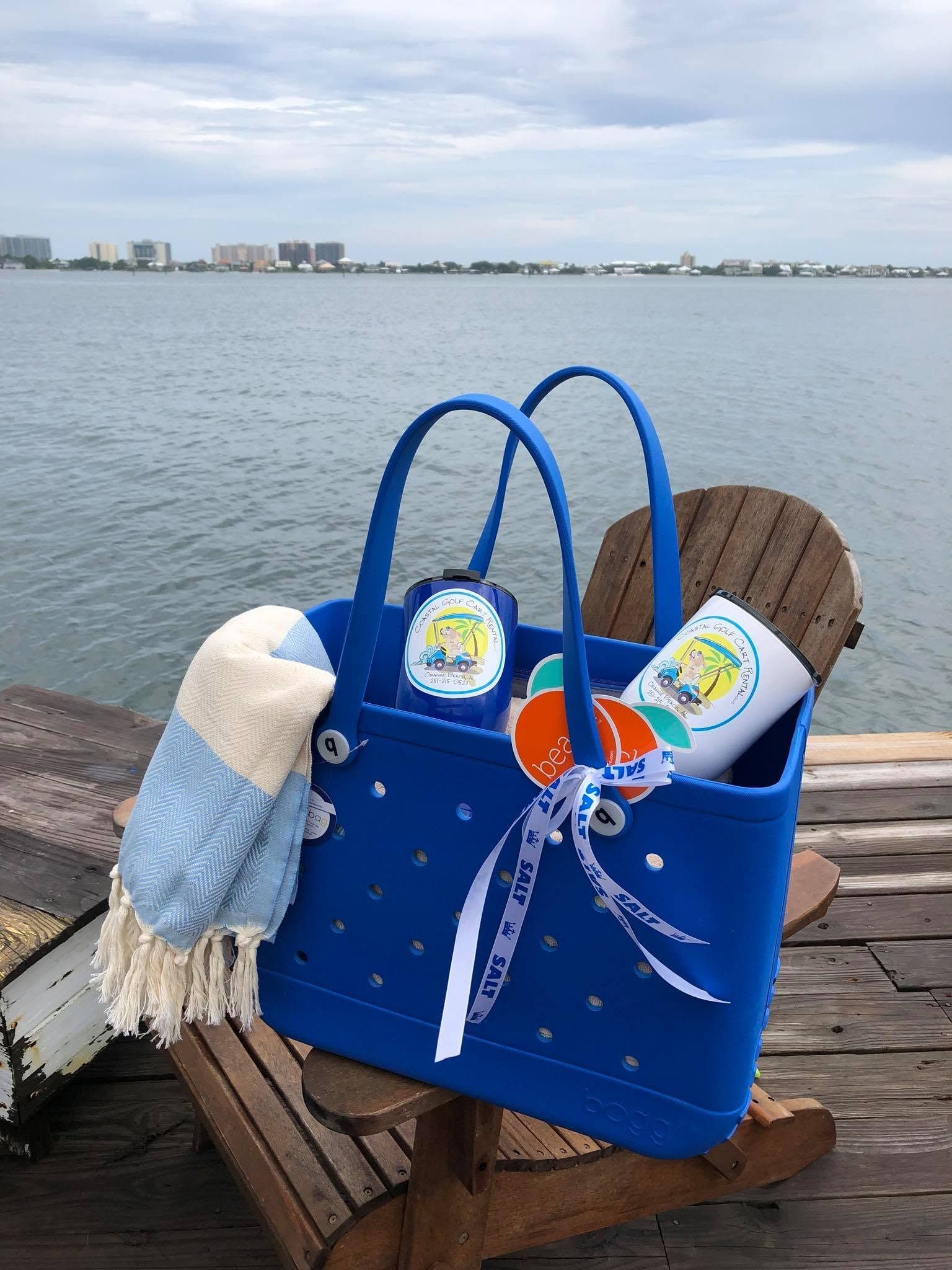 Blue tote bag with towel and drinks on a wooden chair by the waterfront