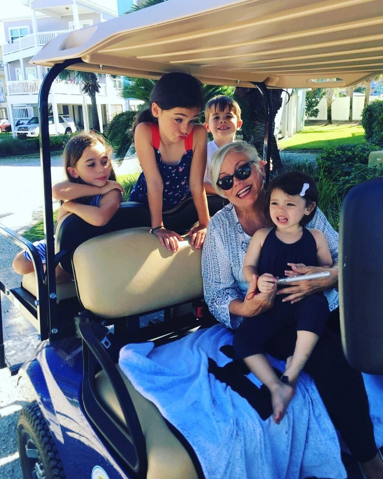 Five people smiling on a golf cart outdoors, with a blue blanket draped over the seat.