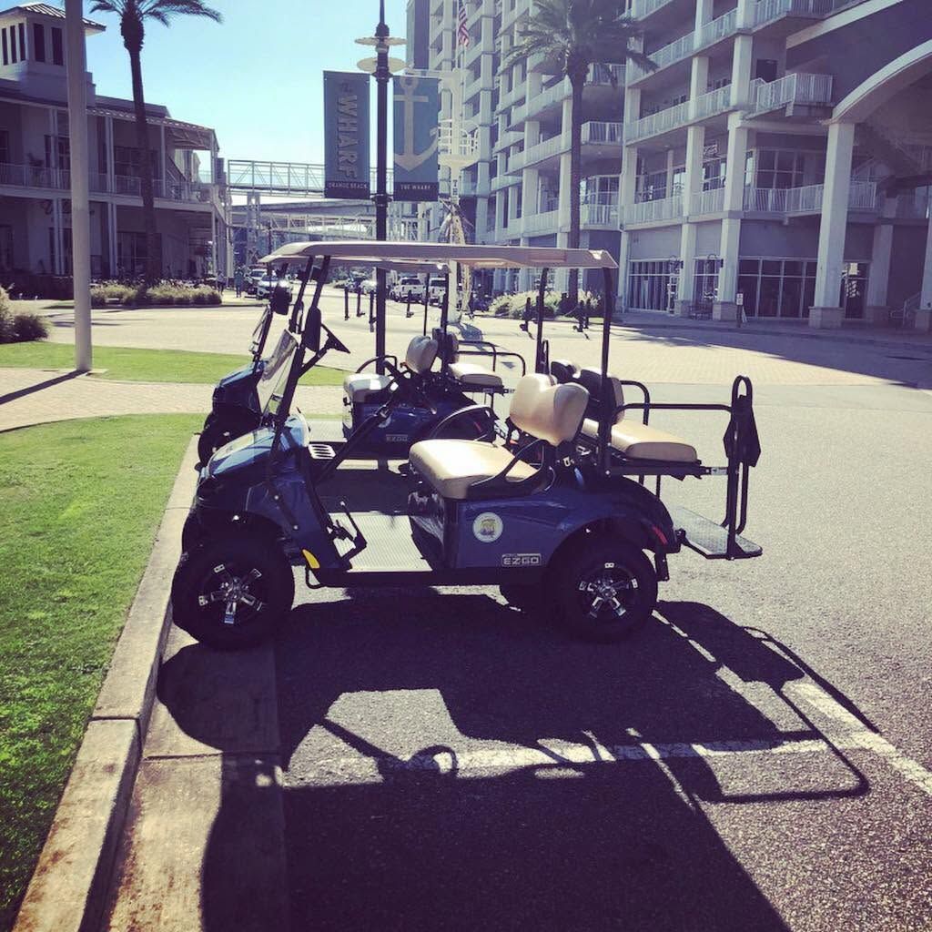 Two black golf carts parked on a sunny resort street with palm trees and buildings nearby