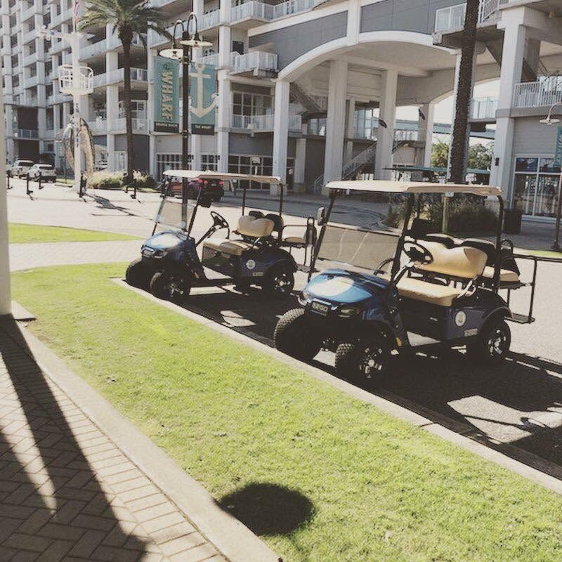 Parked golf carts beside a sunlit sidewalk and modern apartment buildings