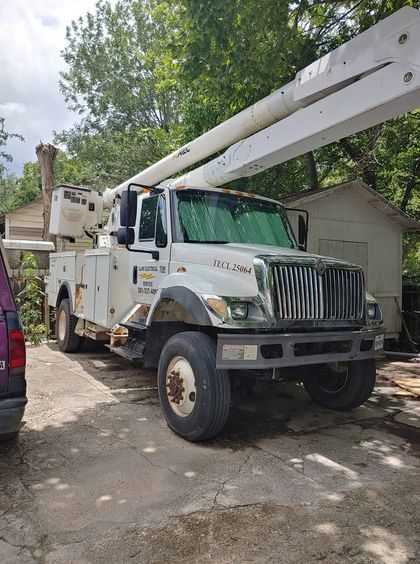 White utility bucket truck parked outdoors on a dirt road near trees and a small shed.