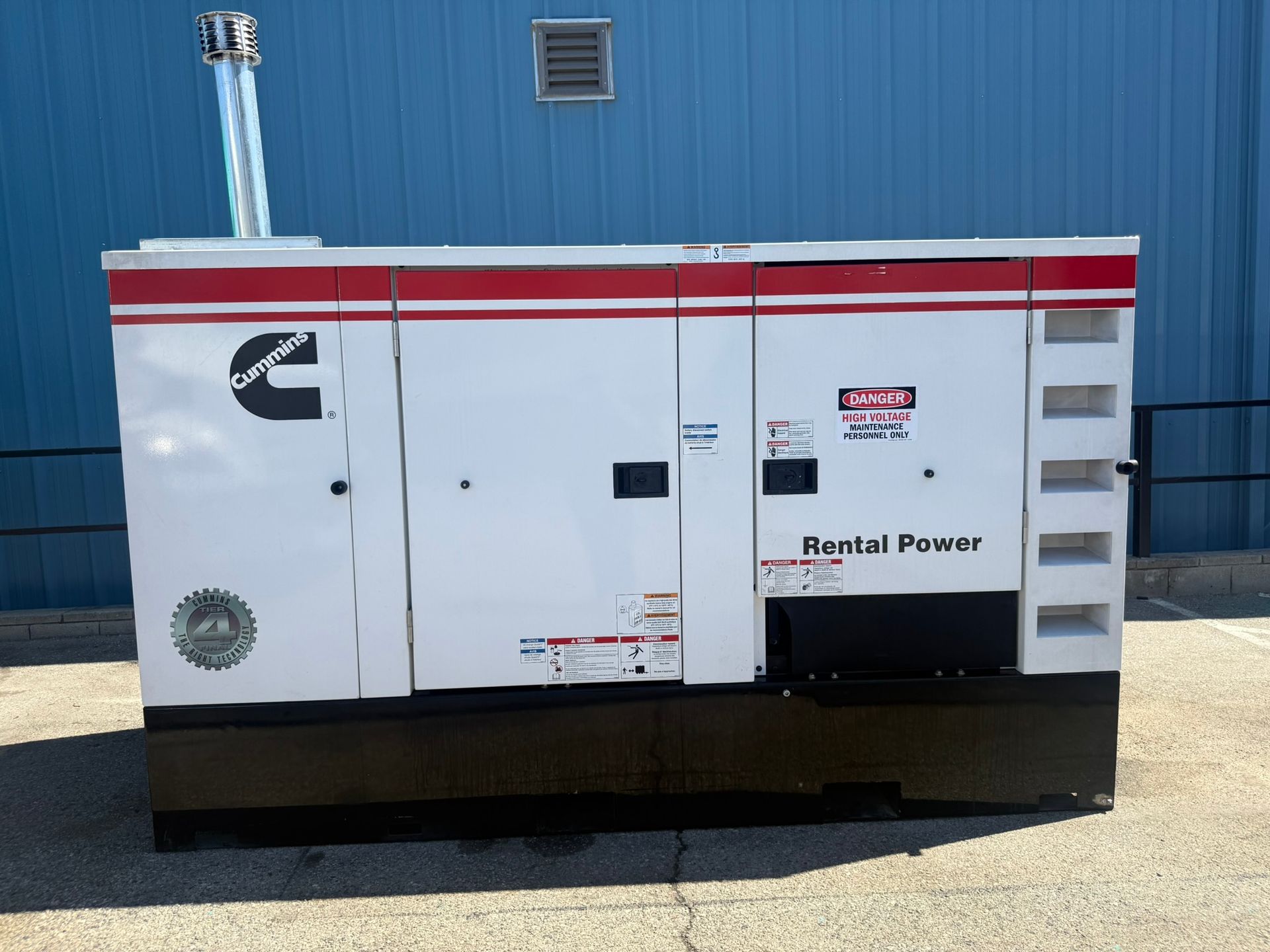 White rental power generator trailer with red stripes parked beside a blue building