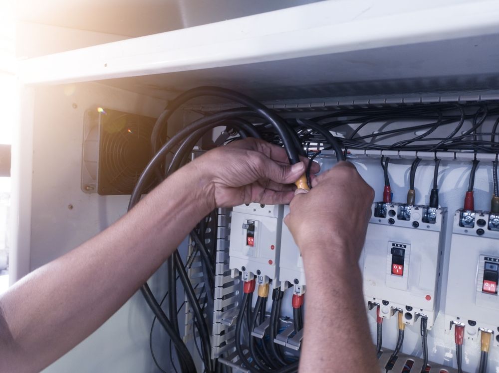 Hands wiring electrical panels inside an open control cabinet.