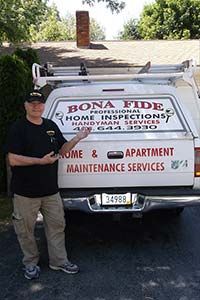 Man in black shirt and cap stands smiling beside a white truck with
