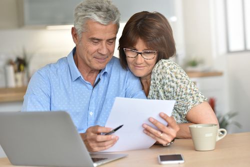 A senior couple reviews paperwork together while seated at a table, appearing focused and engaged in discussion.