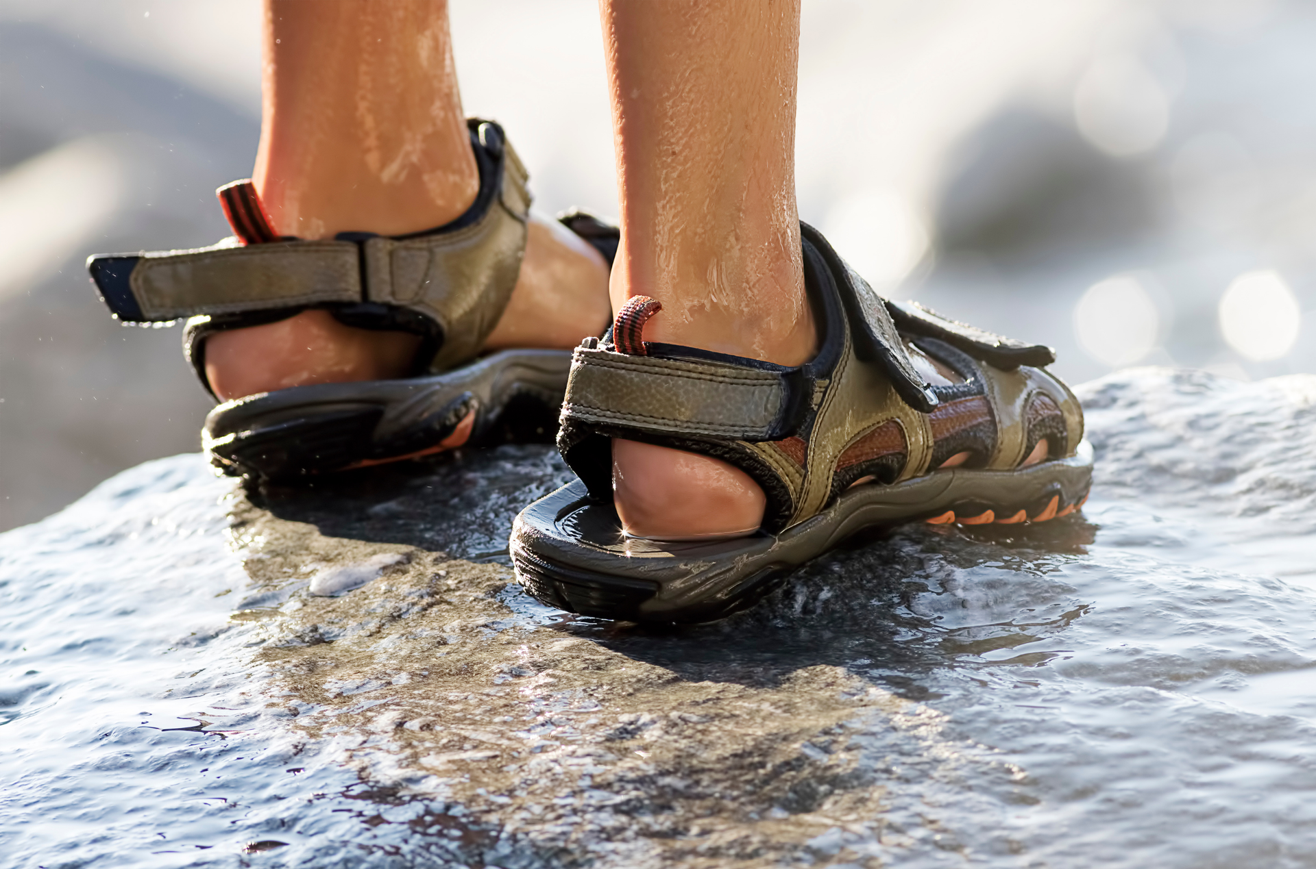 A person wearing sandals is standing on a rock in the water.