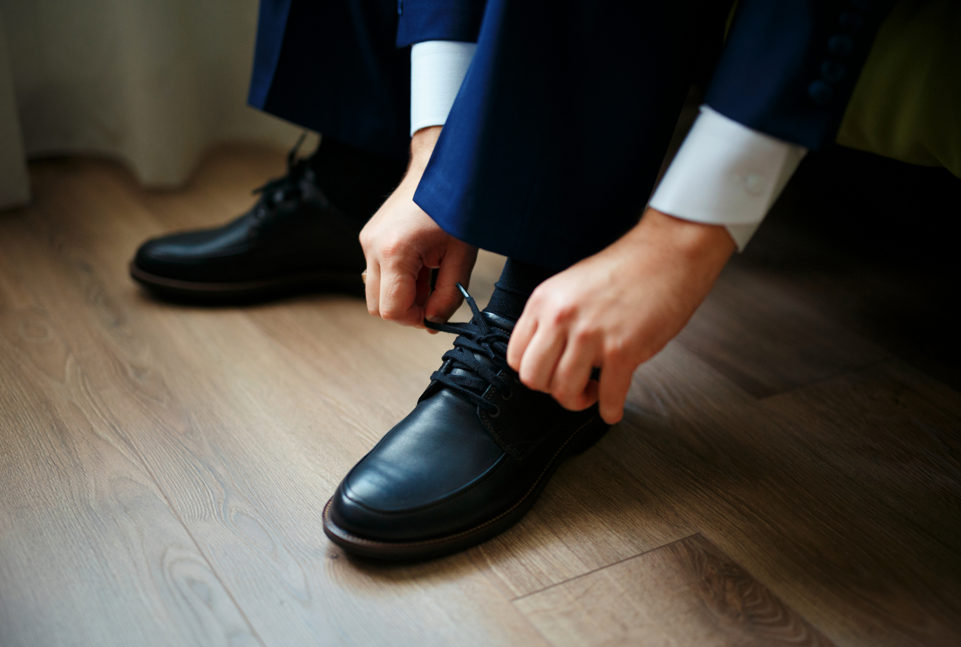 A man in a suit is tying his shoes on a wooden floor.