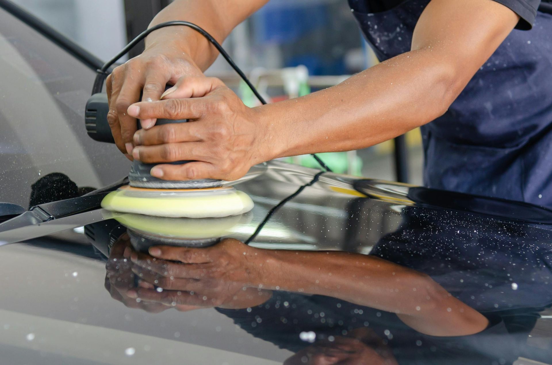 Person polishing a car with an electric buffer in a garage.