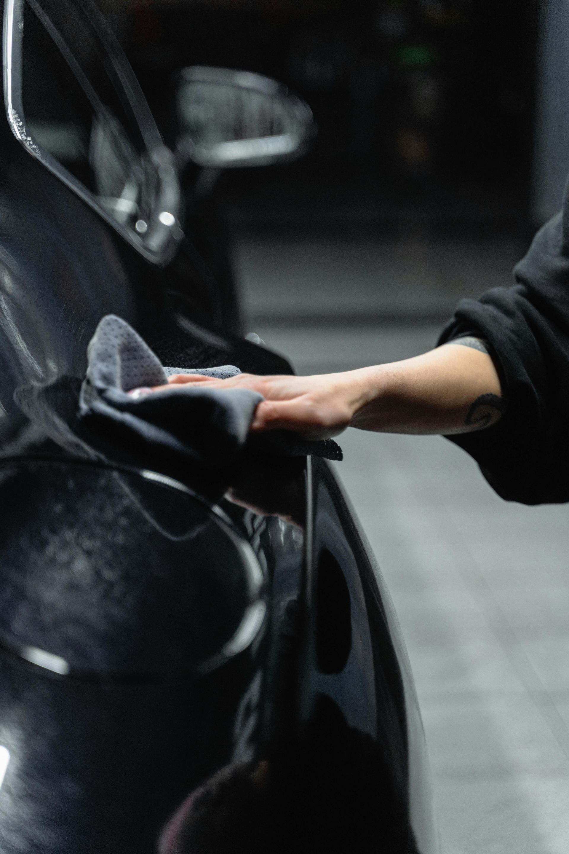 Person wiping down a black car with a gray cloth.