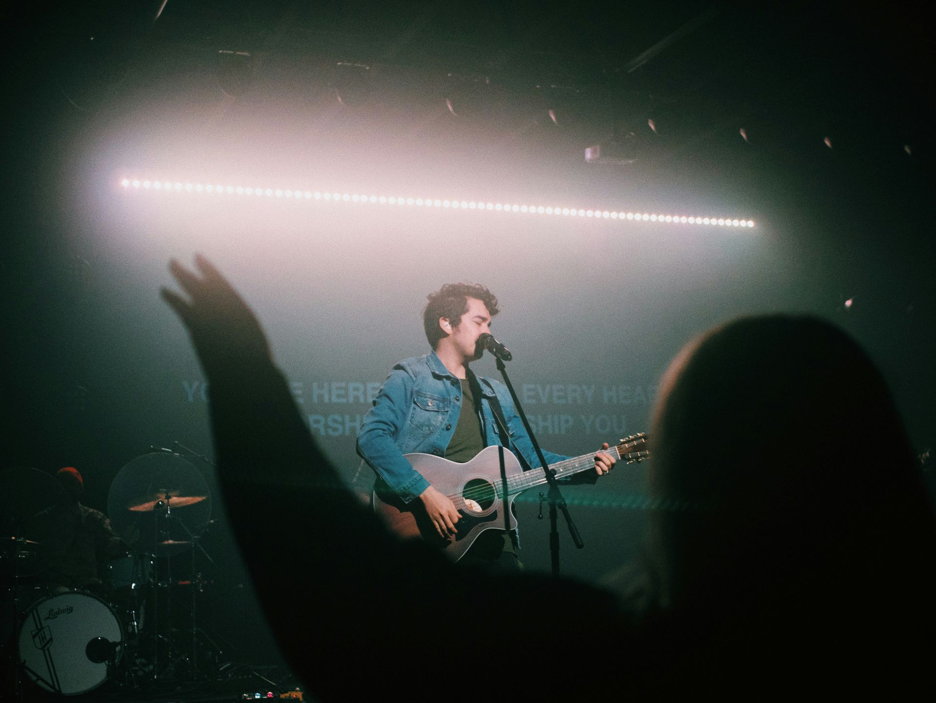 A man is singing into a microphone while playing a guitar on stage.