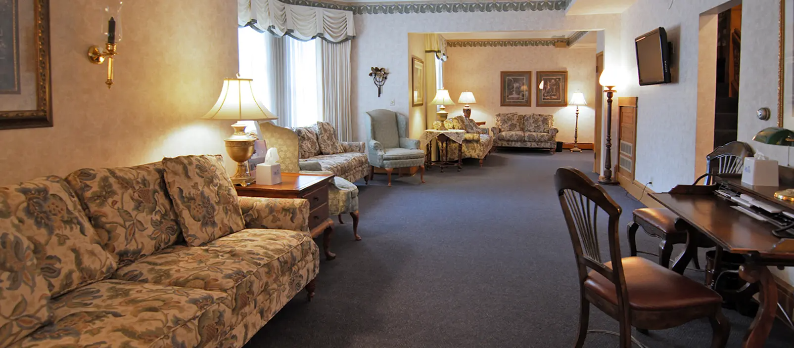 A softly lit funeral home with couches, tables, and a desk. A sense of somber elegance.
