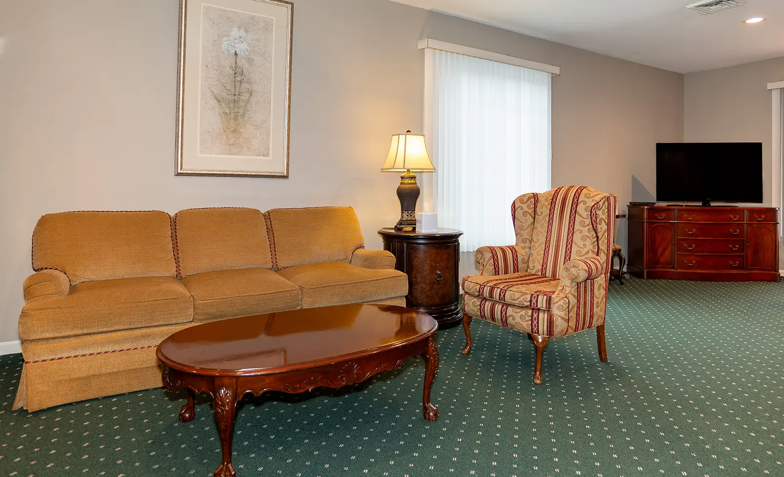 A living room with sofa, armchair, coffee table, lamp, TV, and window; gray walls, green carpet.