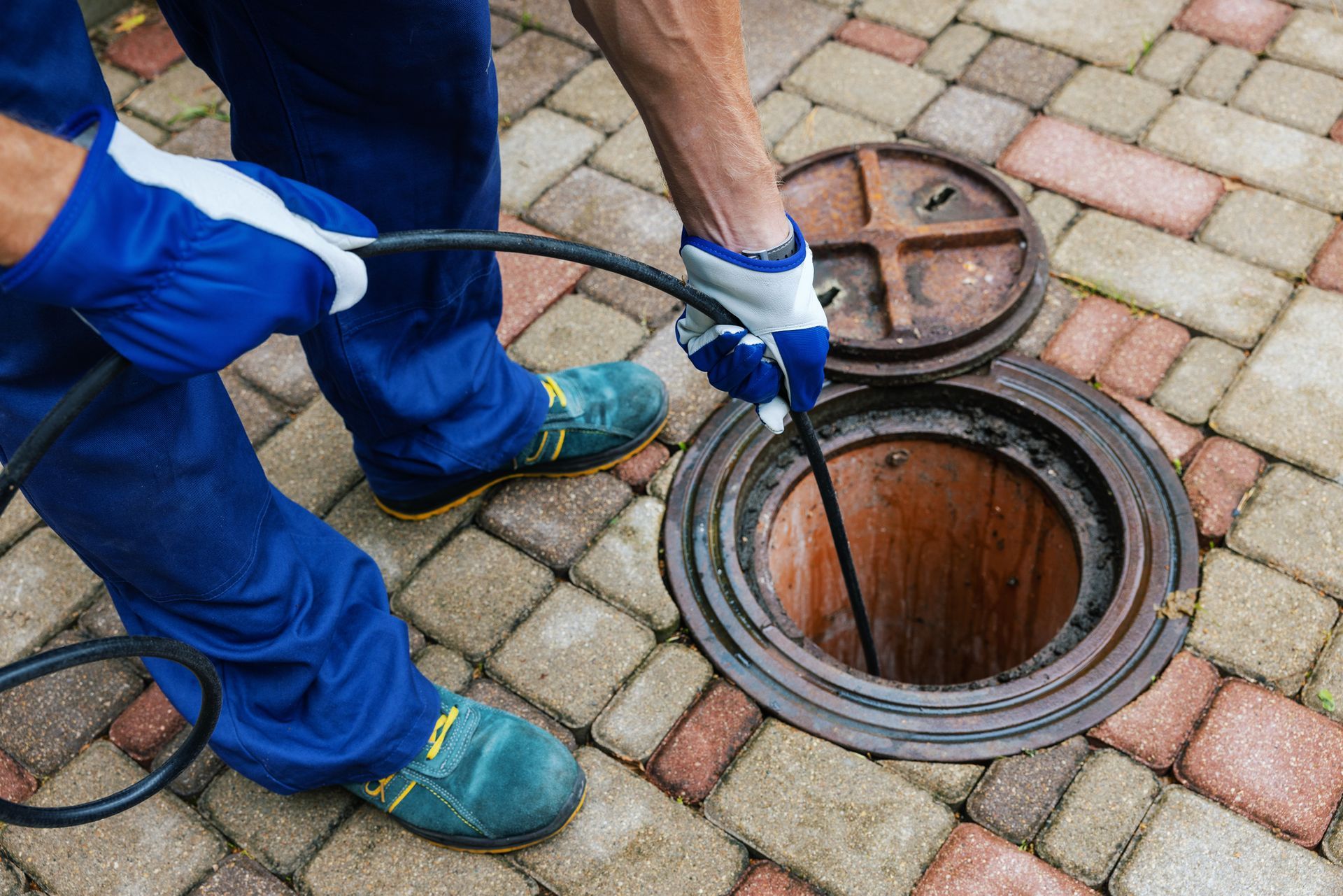 A man is cleaning a manhole cover with a hose.