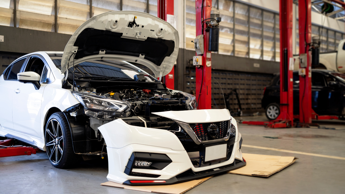A white car with its hood open is being repaired in a garage for auto body repair