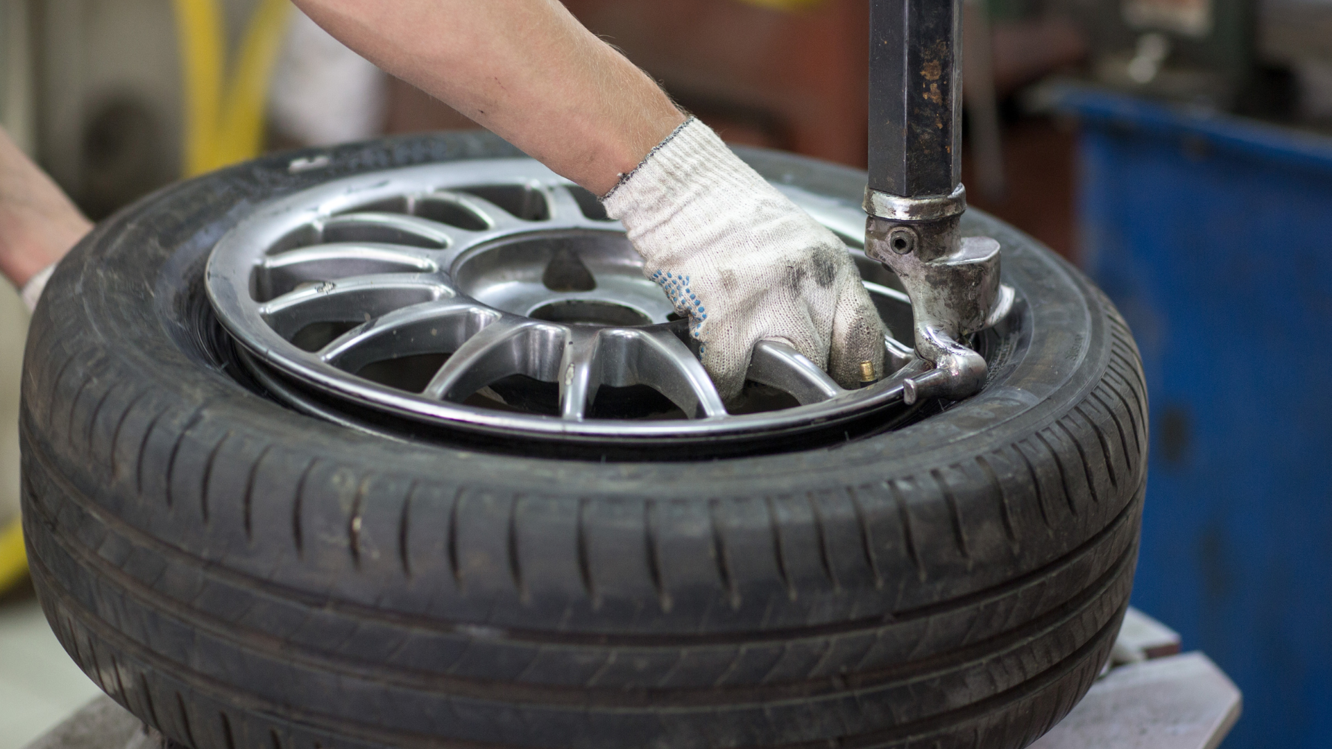 Gloved hands using a tire machine to mount a silver car wheel on a tire.
