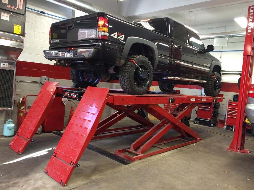 Black pickup truck on a red lift in an auto repair shop